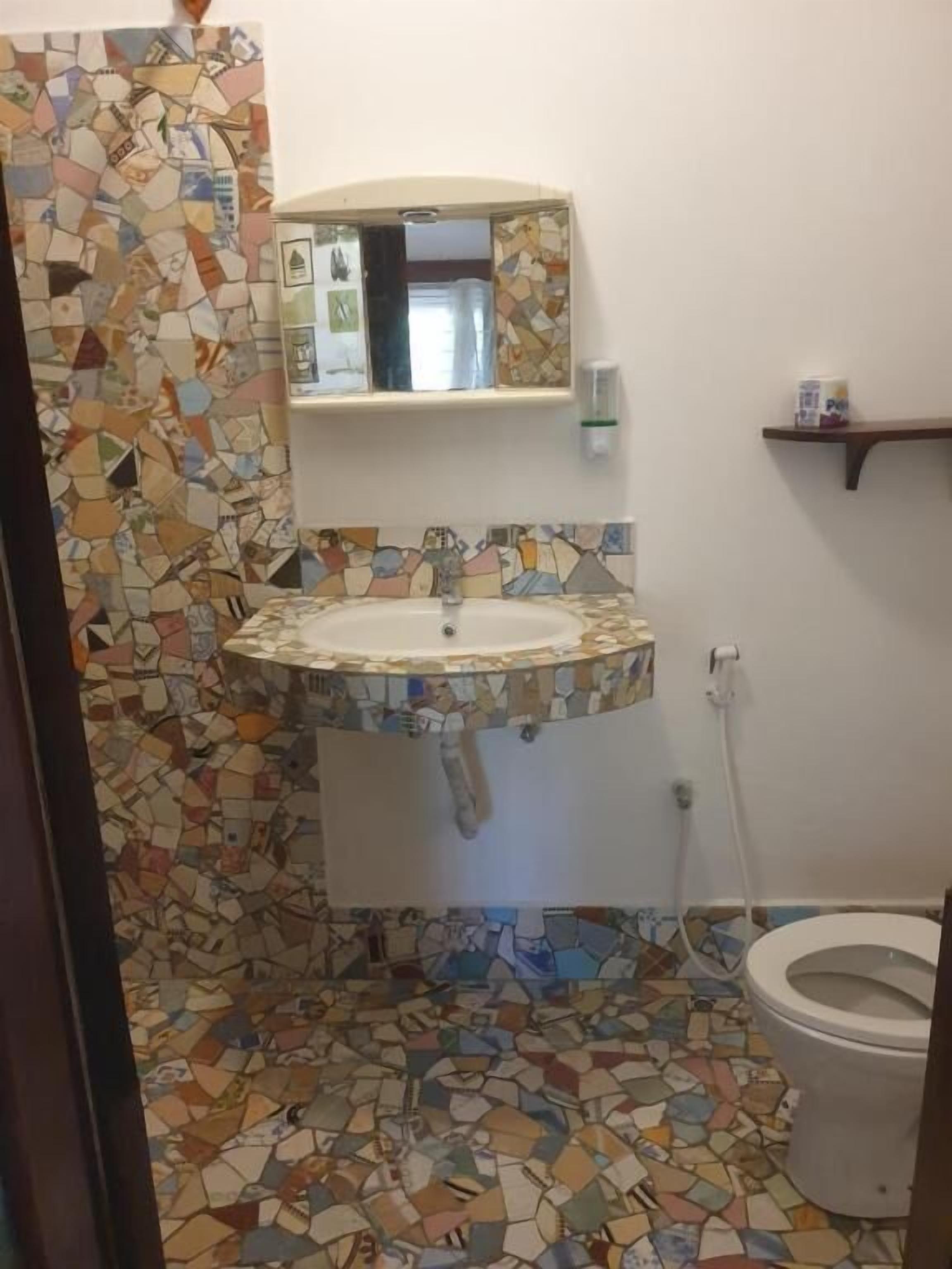 A bathroom with a mosaic tile floor and walls, a sink with a mirror above it, and a toilet.