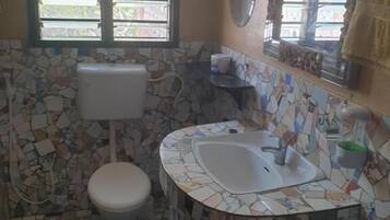 Une salle de bain avec un sol en mosaïque, des toilettes, un lavabo et une fenêtre avec des stores.