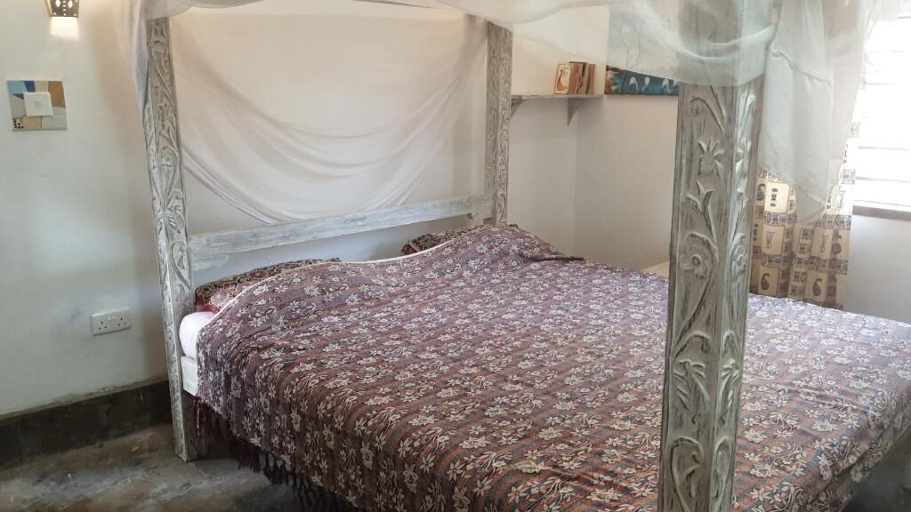 Una habitación con cama con dosel, dosel blanco y colcha estampada.