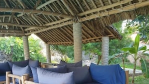 Un espacio de estar al aire libre con bancos acolchados y techo de paja.
