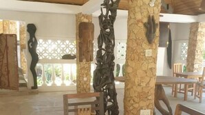 Un espacio interior amplio con una mesa y sillas de madera, pilares de piedra con esculturas y un techo alto con vigas de madera.