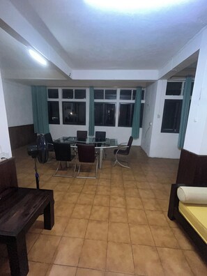 Une pièce spacieuse avec un sol carrelé, une table à manger avec des chaises, un canapé et un ventilateur.