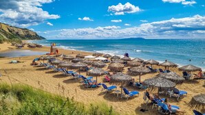 Een strand met rieten parasols en blauwe ligbedden, een wachthuis en een helder uitzicht op de zee.