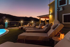 Un espace aménagé au bord de la piscine, avec des chaises longues et une pergola, le tout entouré d’un jardin paysager.