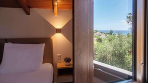 Een slaapkamer met een houten plafond, een bed met witte lakens, een nachtkastje met een lamp, en een raam met uitzicht op een landschap.
