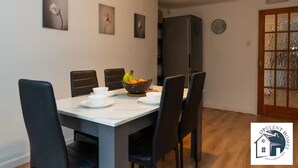 A dining area with a table set for four, a fruit bowl, and a refrigerator in the background.