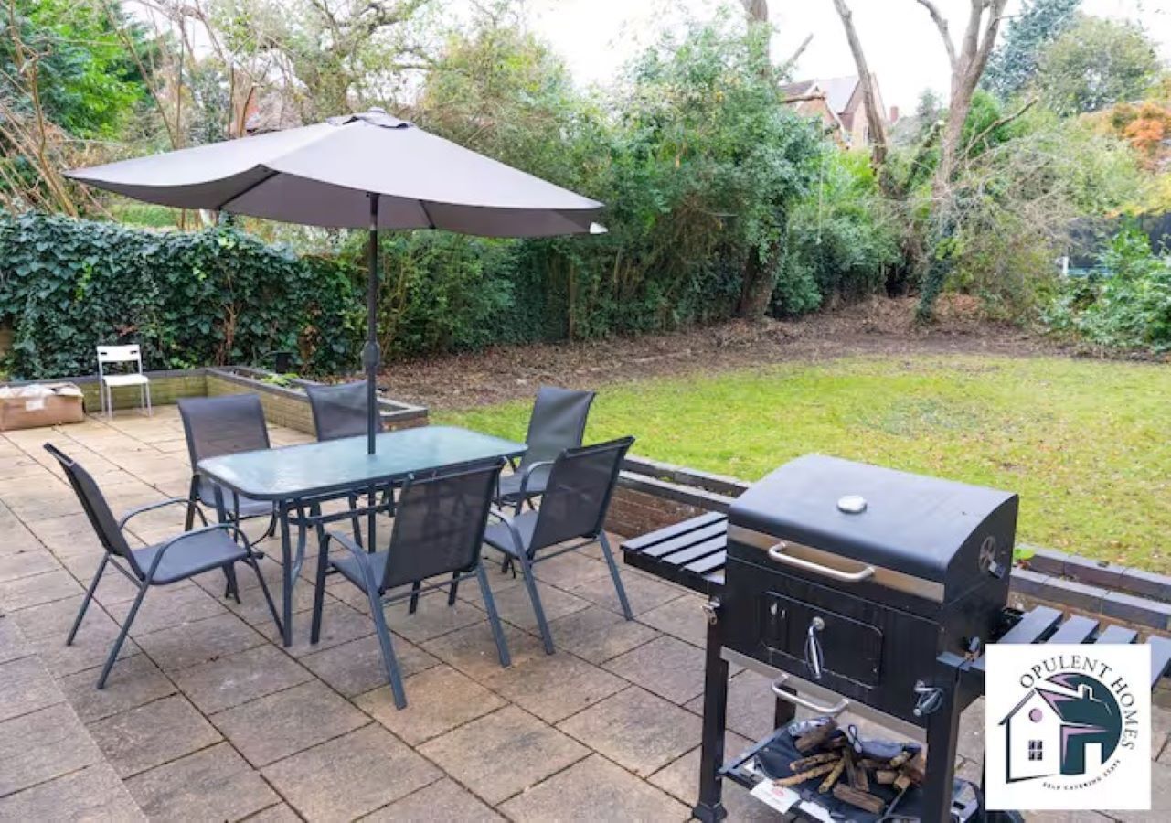 An outdoor patio with a table and chairs, a barbecue grill, and an umbrella.