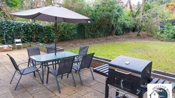 An outdoor patio with a table and chairs, a barbecue grill, and an umbrella.