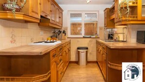 A kitchen with wooden cabinets, a countertop, a sink, and a trash can.