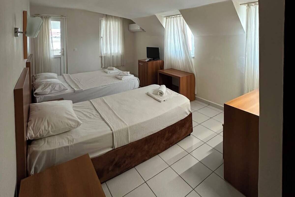 A bedroom with two beds, a wooden nightstand, a bedside table, a TV, and a window with curtains.