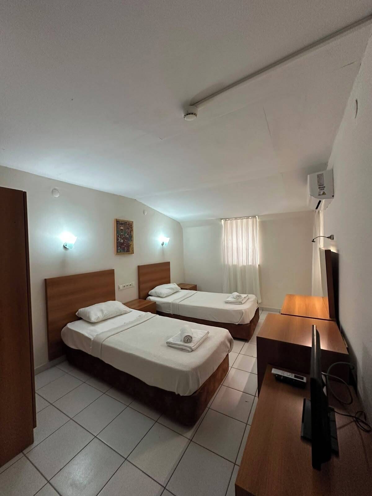 Habitación de hotel con dos camas, un escritorio de madera, un televisor de pantalla plana y un ventilador de techo.