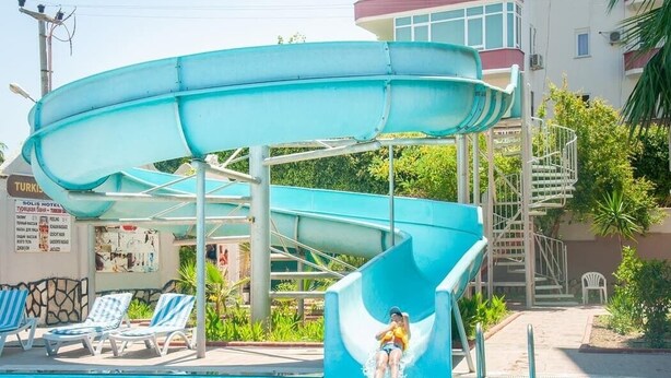 A water slide at a poolside area with lounge chairs and a building in the background.
