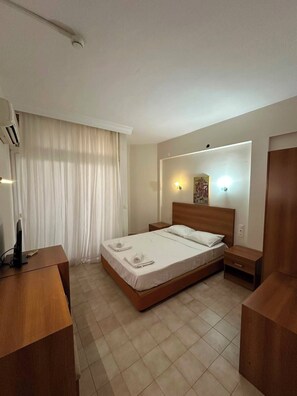 Una camera d'albergo con un letto, comodini, una scrivania, un condizionatore e una finestra con tende.