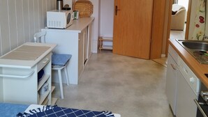 A compact kitchen with a microwave, toaster, and small sink. A wooden door leads to a dining area with a chair and a table. - Beautiful bright 60 sqm apartment near Magdeburg city center and zoo, barrier-free (Magdeburg)