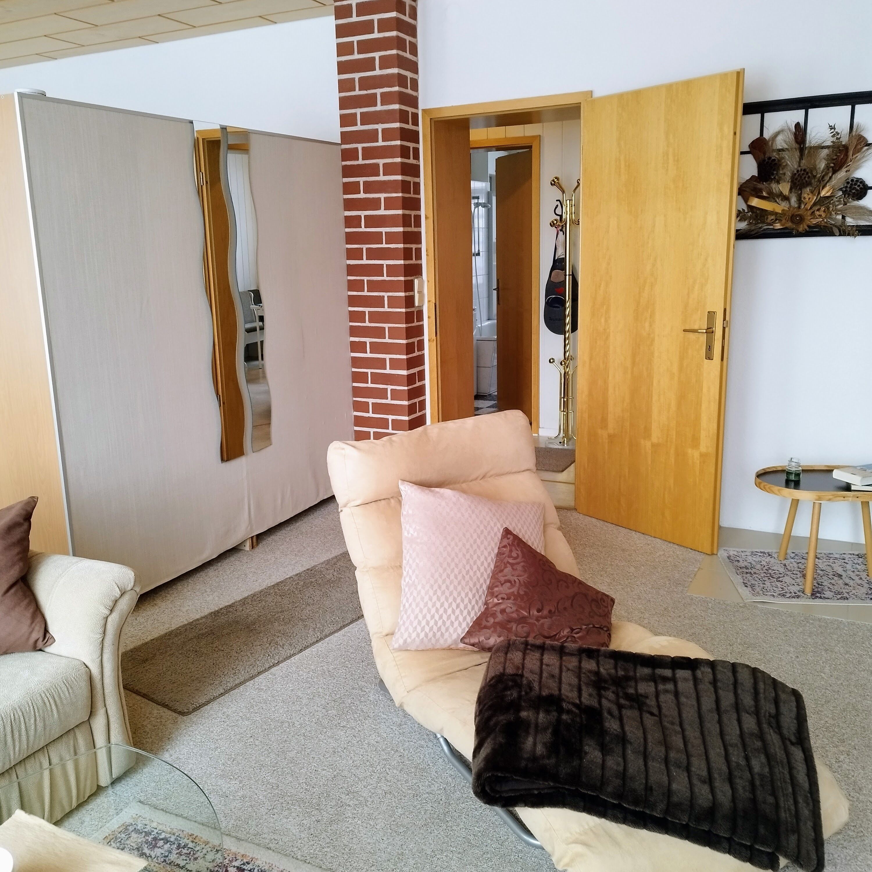 Een woonkamer met een beige bank, een salontafel en een open haard. Er is een deur naar een badkamer en een gang.