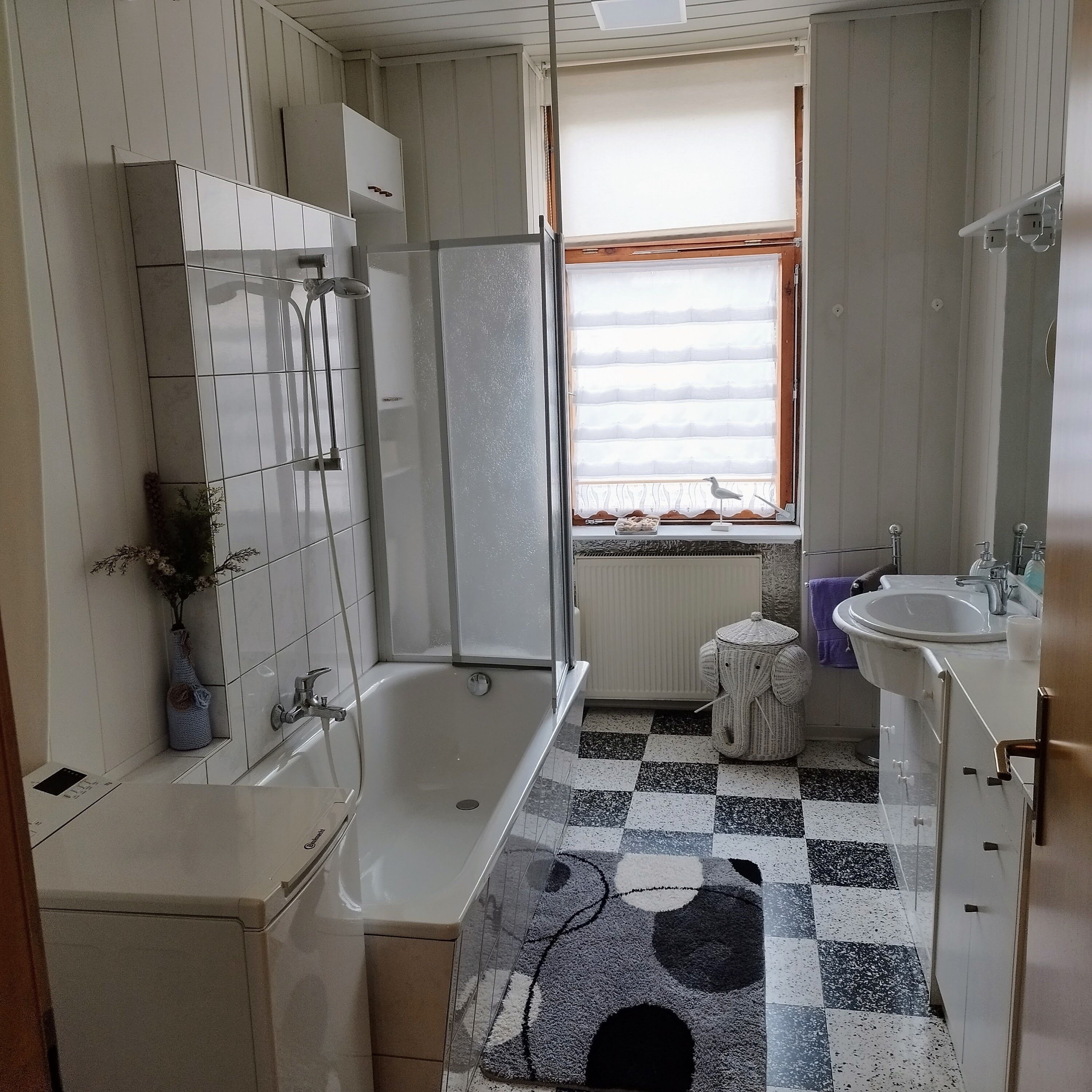 Une salle de bain avec une baignoire, un lavabo et une fenêtre avec des stores.