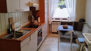 A compact kitchen with white cabinets, a sink, and a window with sheer curtains. - Beautiful bright 60 sqm apartment near Magdeburg city center and zoo, barrier-free (Magdeburg)