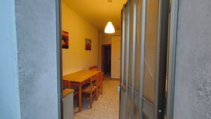 Un pasillo estrecho con una mesa de comedor de madera y sillas, una lámpara colgante y un refrigerador al fondo.