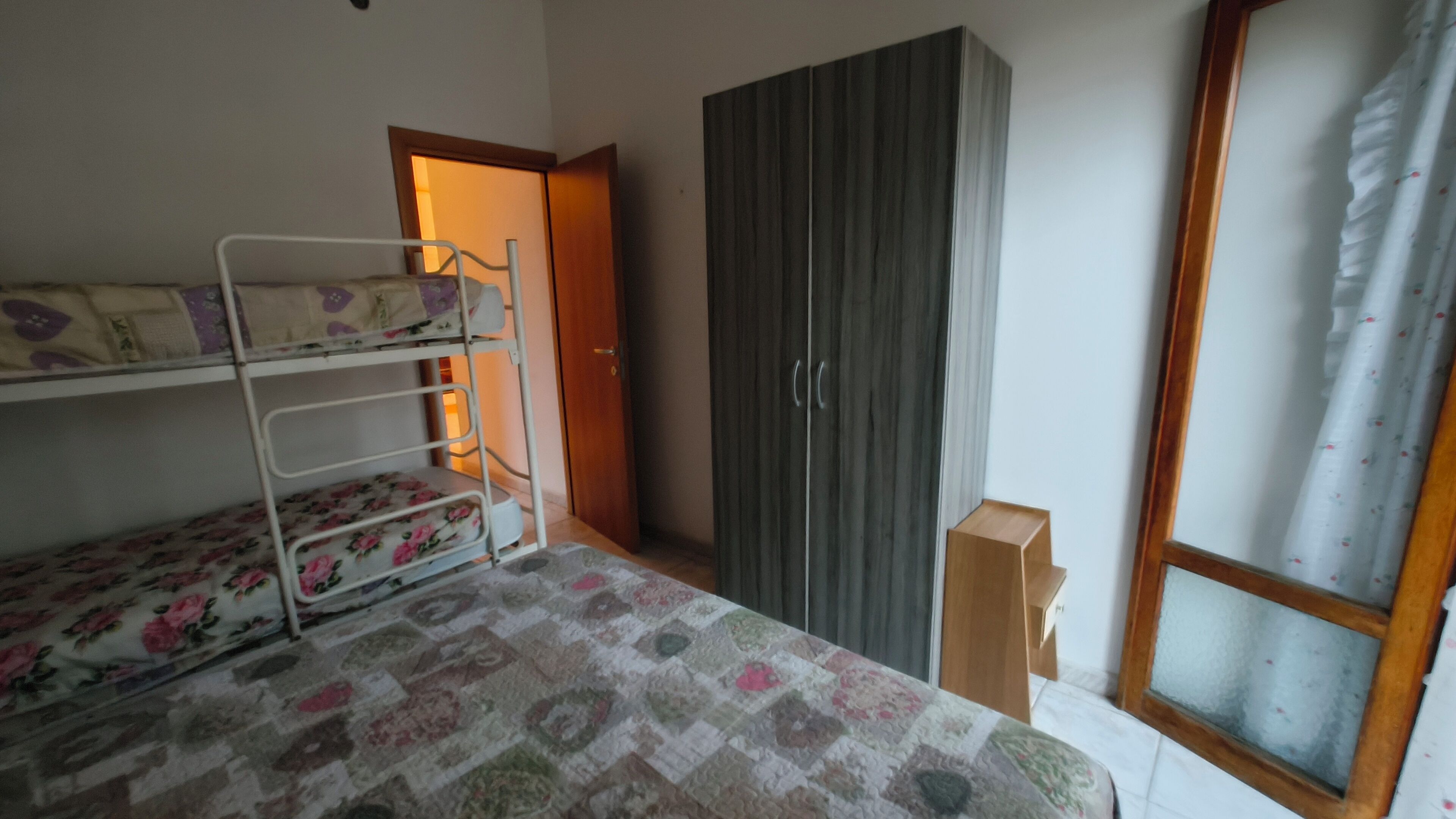 Een kamer met een stapelbed, een kledingkast en een raam met gordijnen.