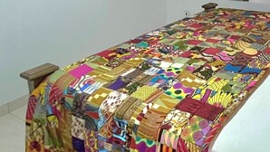 A bedroom with a colorful quilted bedspread, a painting on the wall, and a mirror. - Aburi Emerald Garden Retreat (Aburi)