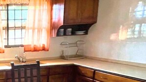 A kitchen with wooden cabinets, a dining table, and a window with curtains. - Aburi Emerald Garden Retreat (Aburi)