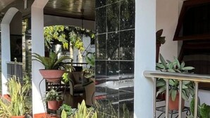 A covered outdoor area with tiled walls, potted plants, and a metal railing. - Aburi Emerald Garden Retreat (Aburi)