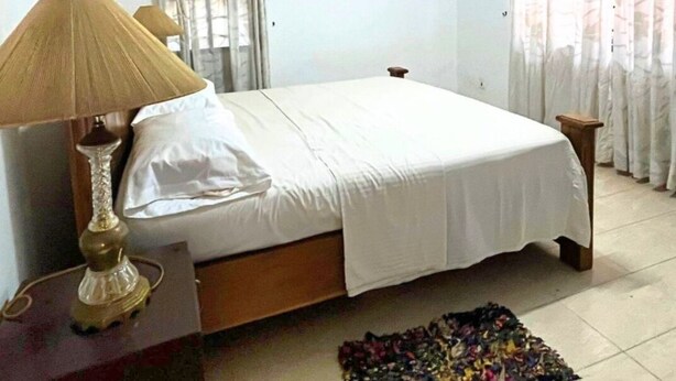 A bedroom with a bed, a bedside table with a lamp, curtains, and a tiled floor. - Aburi Emerald Garden Retreat (Aburi)