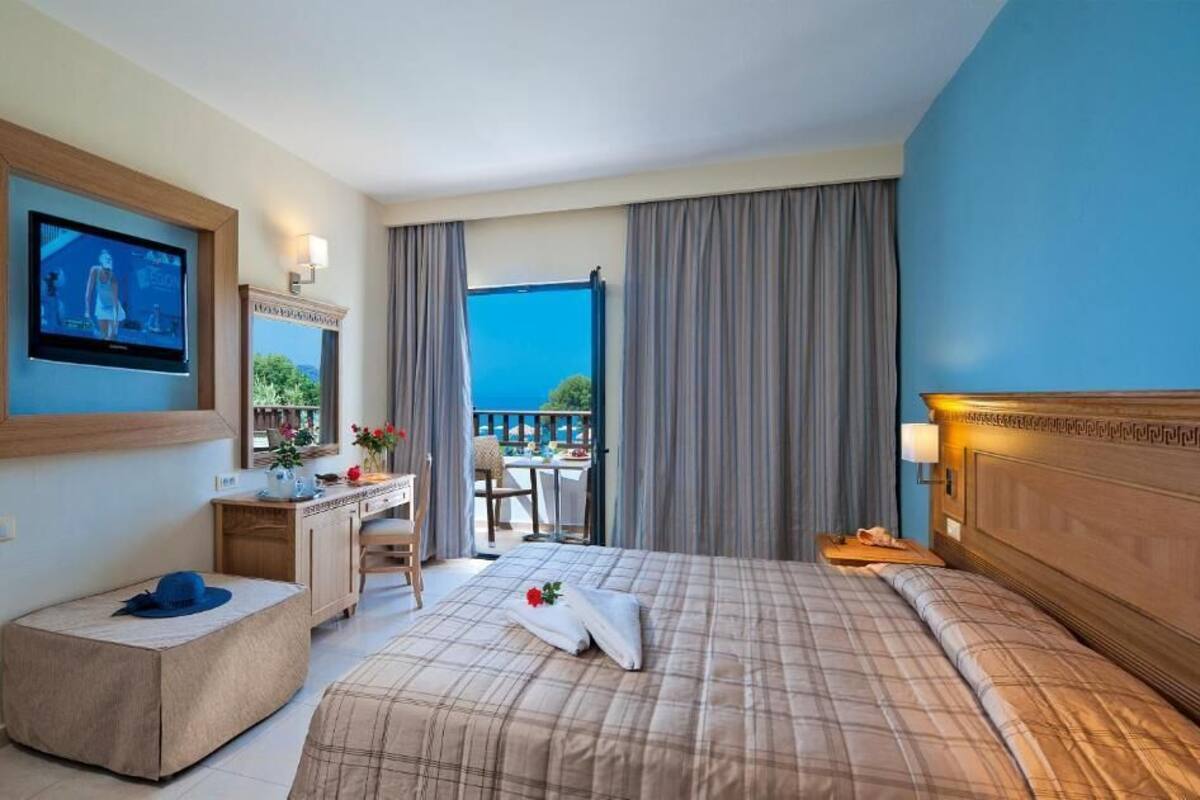 A hotel room with a bed, a desk, a television, and a balcony with a view.