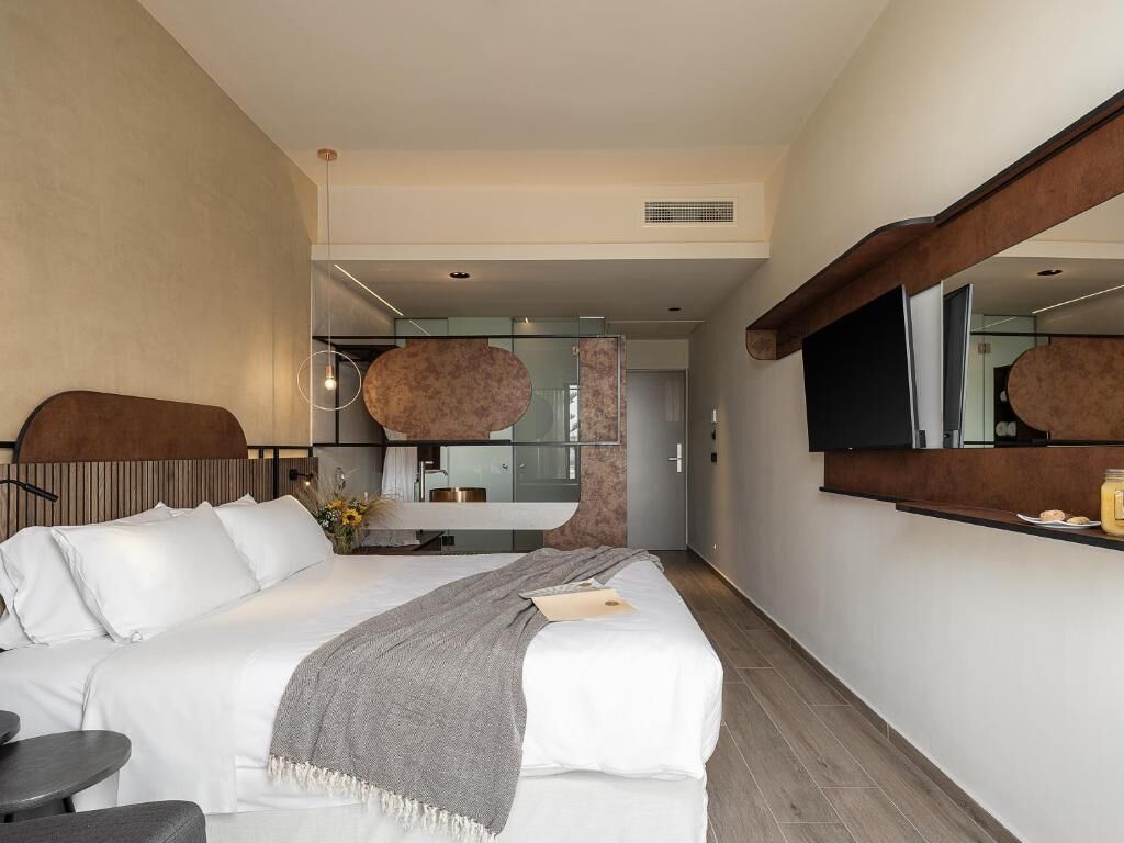 Habitación de hotel moderna con una cama grande, una mesita, un espejo y vistas al baño y la cocina.