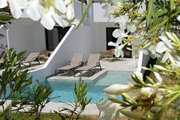 A pool area with lounge chairs and a table, surrounded by white flowers and greenery. - Geraniotis Beach (Platanias)