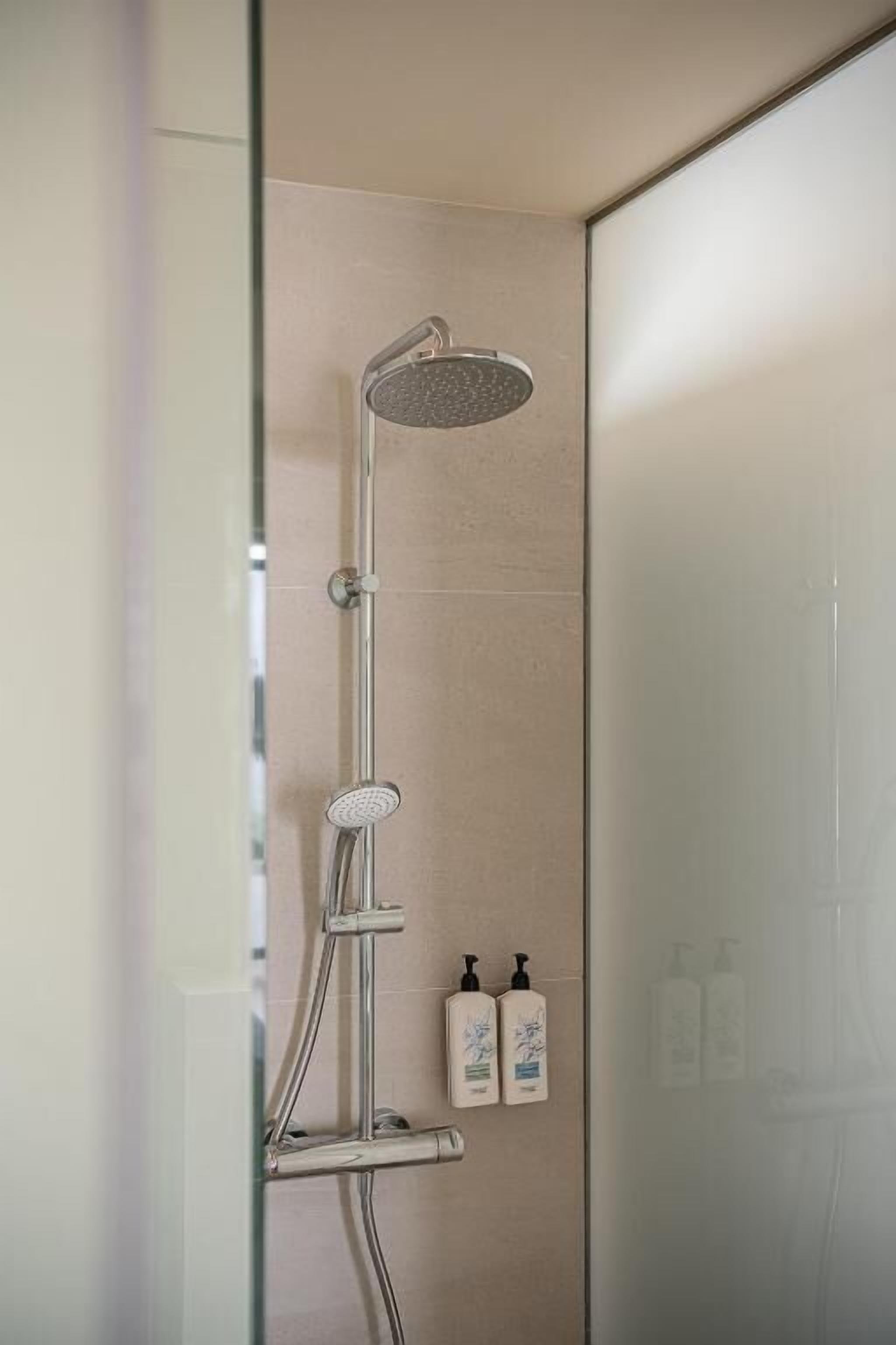 Ducha moderna con cabezal de ducha de lluvia y cabezal de ducha manual, montada en una pared con puerta de vidrio esmerilado.