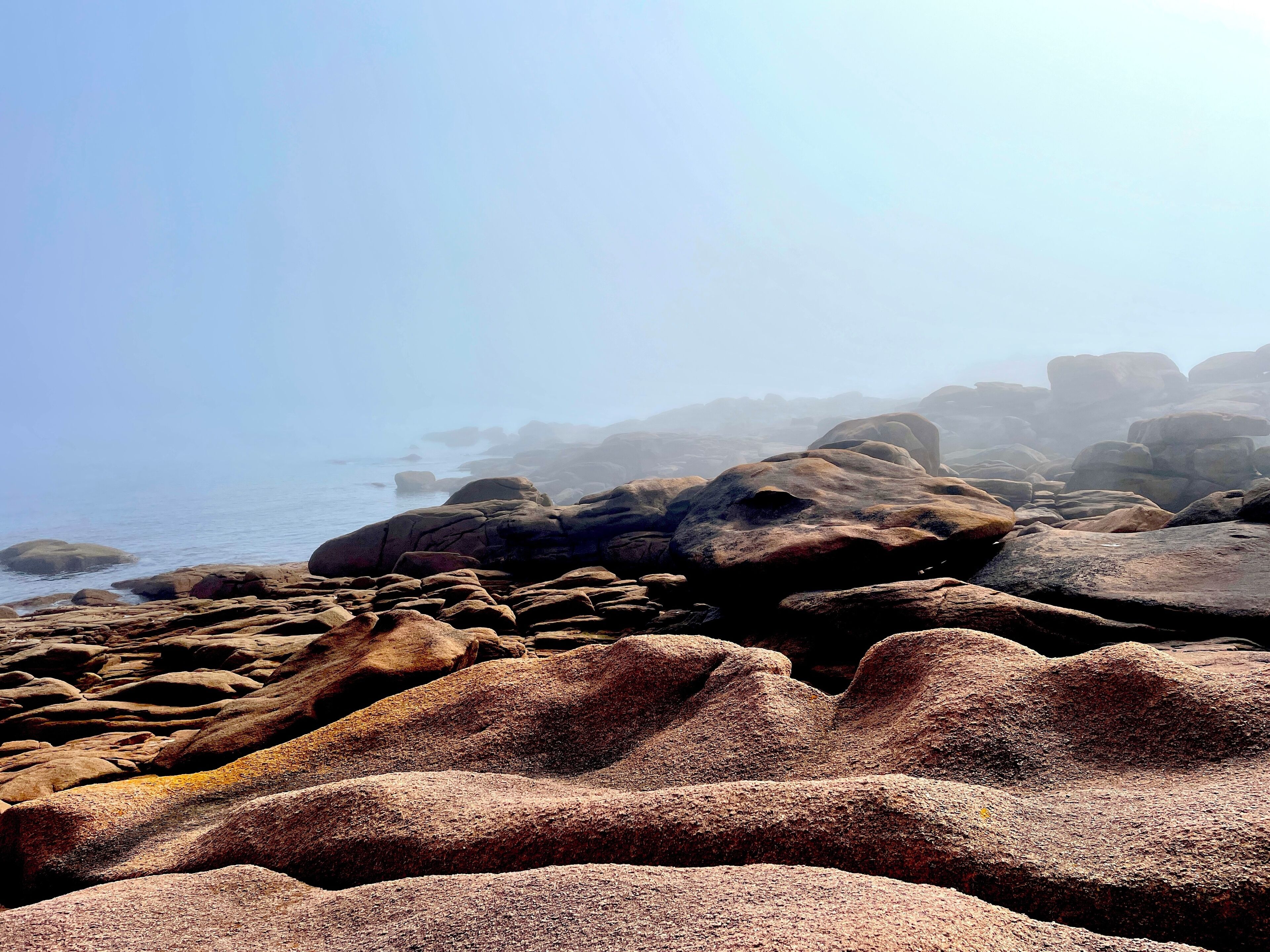 A rocky coastal landscape with large boulders and a calm sea.