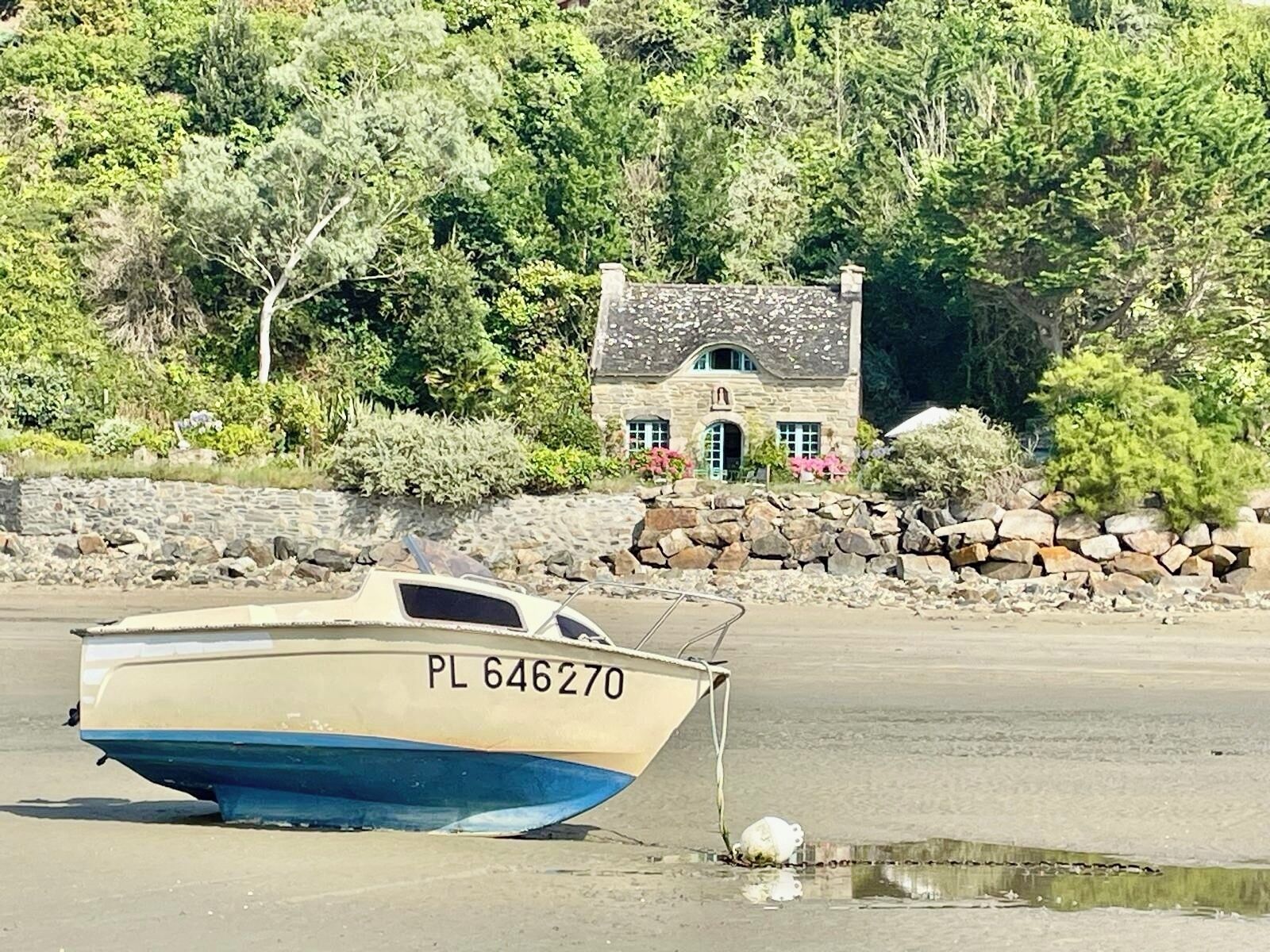 Un bateau portant le numéro d’immatriculation PL 646270, échoué sur une plage de sable, avec un mur de pierres et de la végétation en arrière-plan.