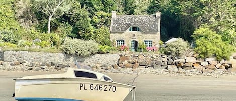 Un bateau portant le numéro d’immatriculation PL 646270, échoué sur une plage de sable, avec un mur de pierres et de la végétation en arrière-plan.