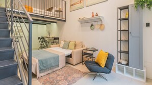 Uma sala de estar moderna com escada, um sofá, uma poltrona, uma mesinha e uma estante de livros.