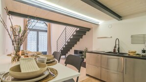 Uma cozinha moderna com eletrodomésticos de aço inoxidável, um espaço de jantar com mesa branca posta para quatro pessoas e uma escada que leva a outro andar.