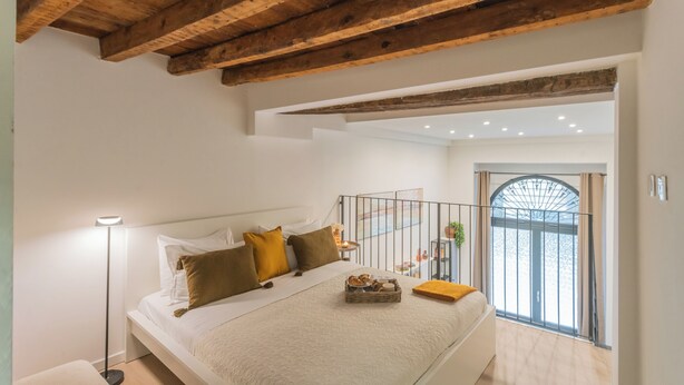 Quarto com cama grande, abajur e vista para uma varanda.