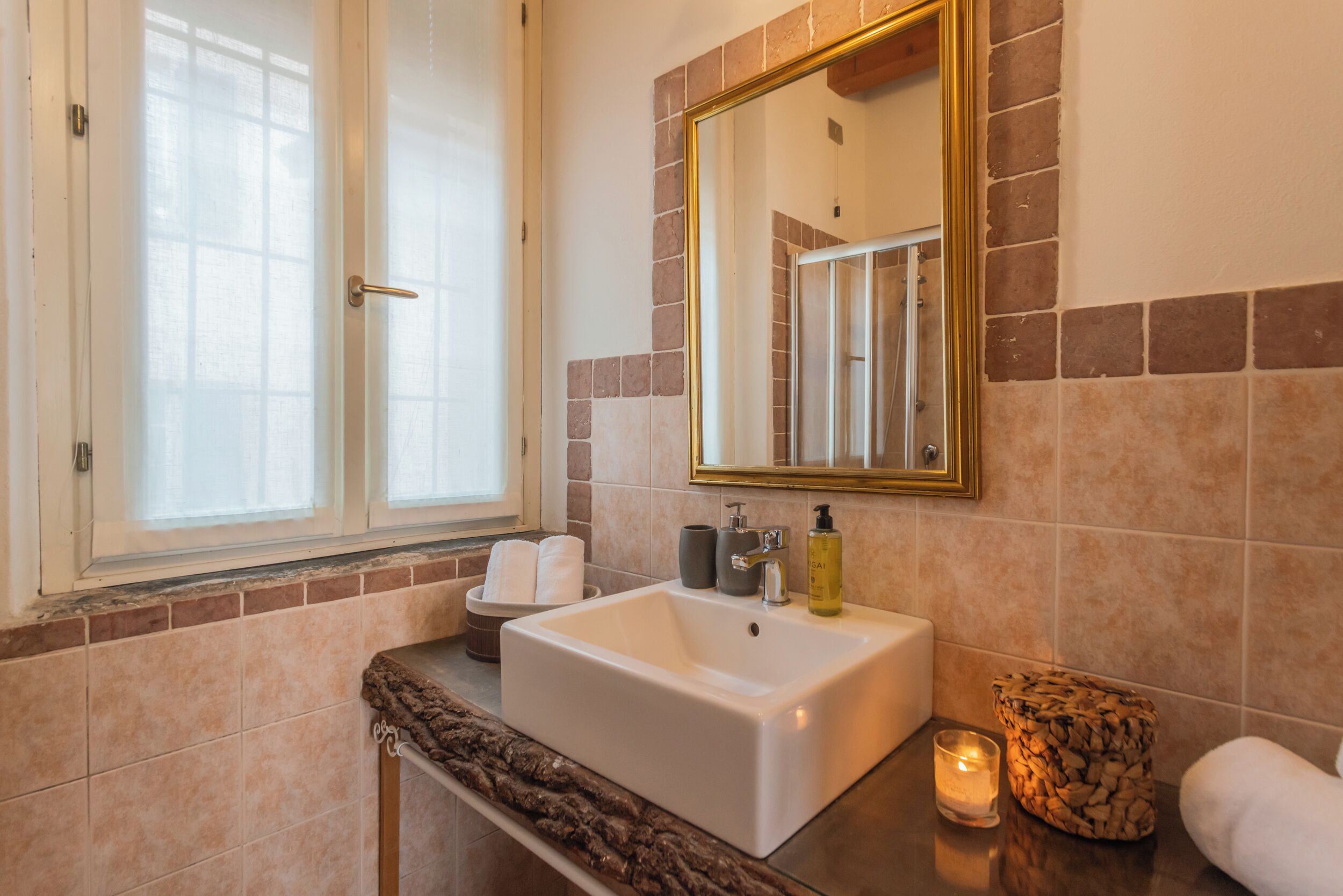 A bathroom with a white sink, a mirror with a gold frame, and a window.