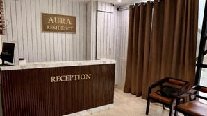 A reception desk labeled "RECEPTION" at AURA RESIDENCY, with a wooden panel backdrop and a computer monitor. - Hotel Aura Residency (Bengaluru)