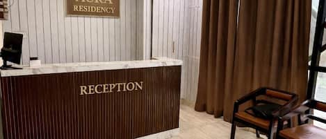 Un mostrador de recepción identificado con la etiqueta "RECEPTION" en AURA RESIDENCY, con un panel de madera como fondo y un monitor de computadora.