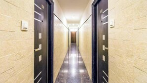 A long, narrow hallway with dark doors on both sides, leading to a bright room at the end. - Hotel Aura Residency (Bengaluru)