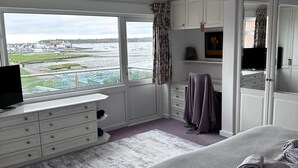 A bedroom with a large bed, a dresser, a television, and a window with a view of the sea. - Mudeford, Dorset. Spectacular Seafront Views. Perfect Family Getaway. Driveway. (Christchurch)
