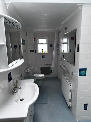 A bathroom with white tiles, a sink, a toilet, a window, and a mirror.