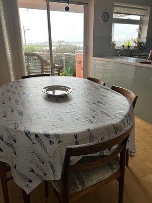A dining area with a round table covered by a tablecloth with a fish pattern, surrounded by wooden chairs.