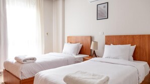 Een hotelkamer met twee bedden, witte lakens, houten hoofdborden, een bedlampje en een lijst met een afbeelding aan de muur.