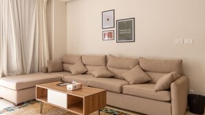 Een moderne woonkamer met een beige hoekbank, een houten salontafel en een kamerbreed tapijt met dessin.