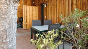 Een buiteneetgedeelte met een houten tafel en stoelen, omringd door potplanten en een boomstam.