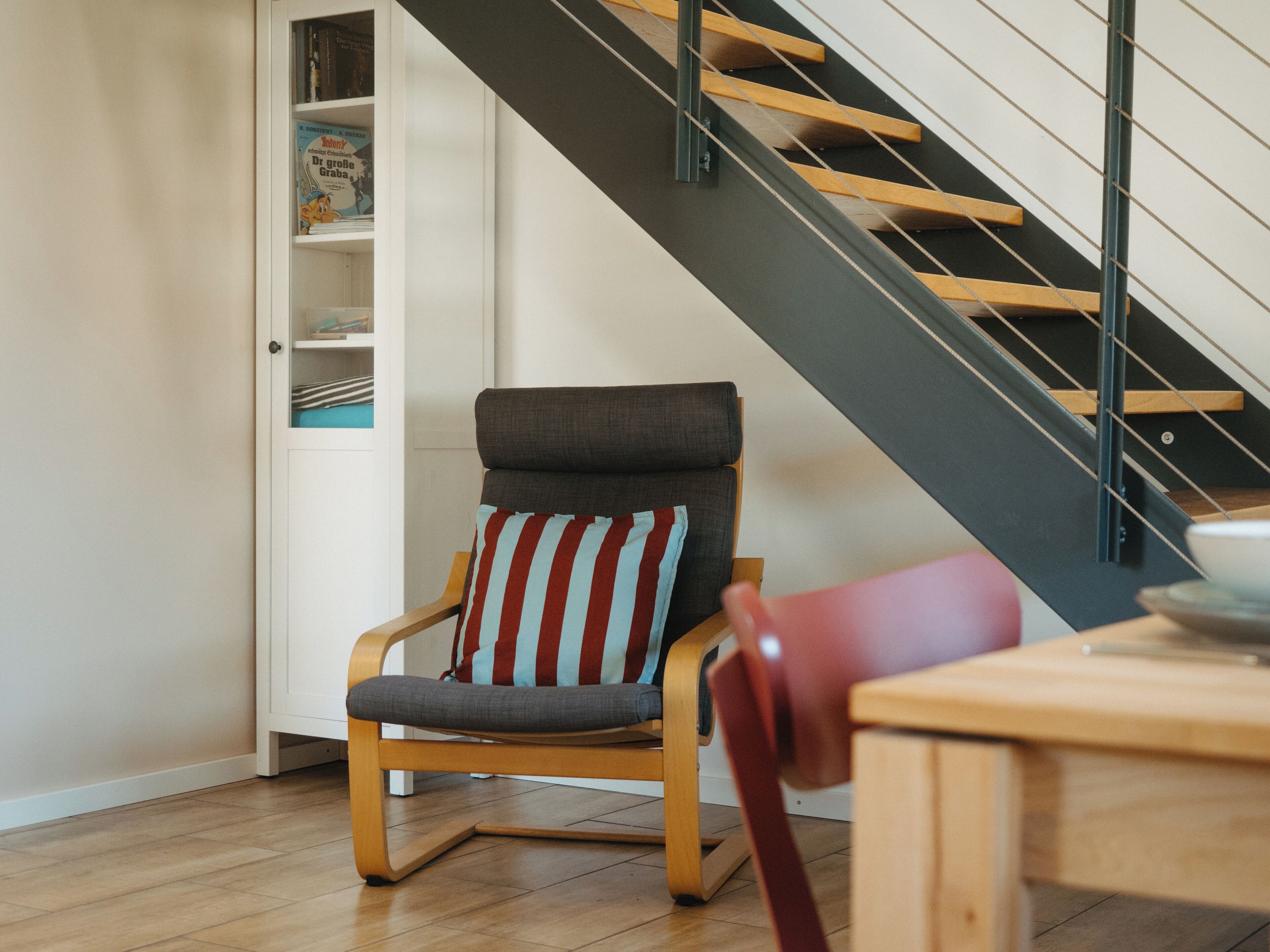 A chair with a striped cushion, a wooden table, and a staircase with a black railing.