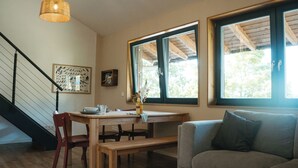 Een eethoek met een houten tafel, stoelen en een bank. Er is een trap met een leuning, een bank en een raam met uitzicht op bomen.