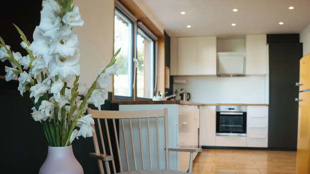 Een moderne keuken met witte kasten, een houten stoel en een vaas witte bloemen op een tafel.